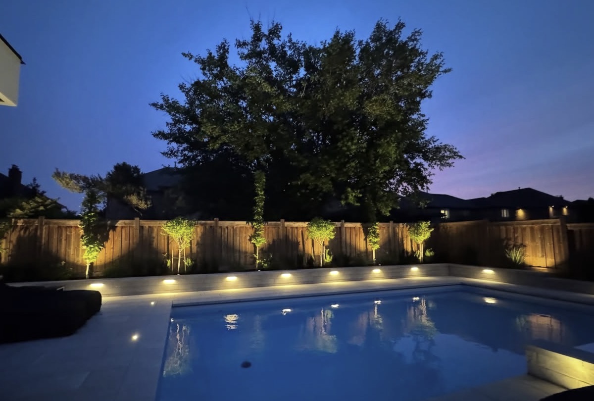 Modern pool with warm cove lighting along a fence at dusk